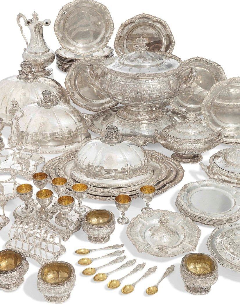 A laid-out service of antique silver — teapot, plates, goblets, flatware
